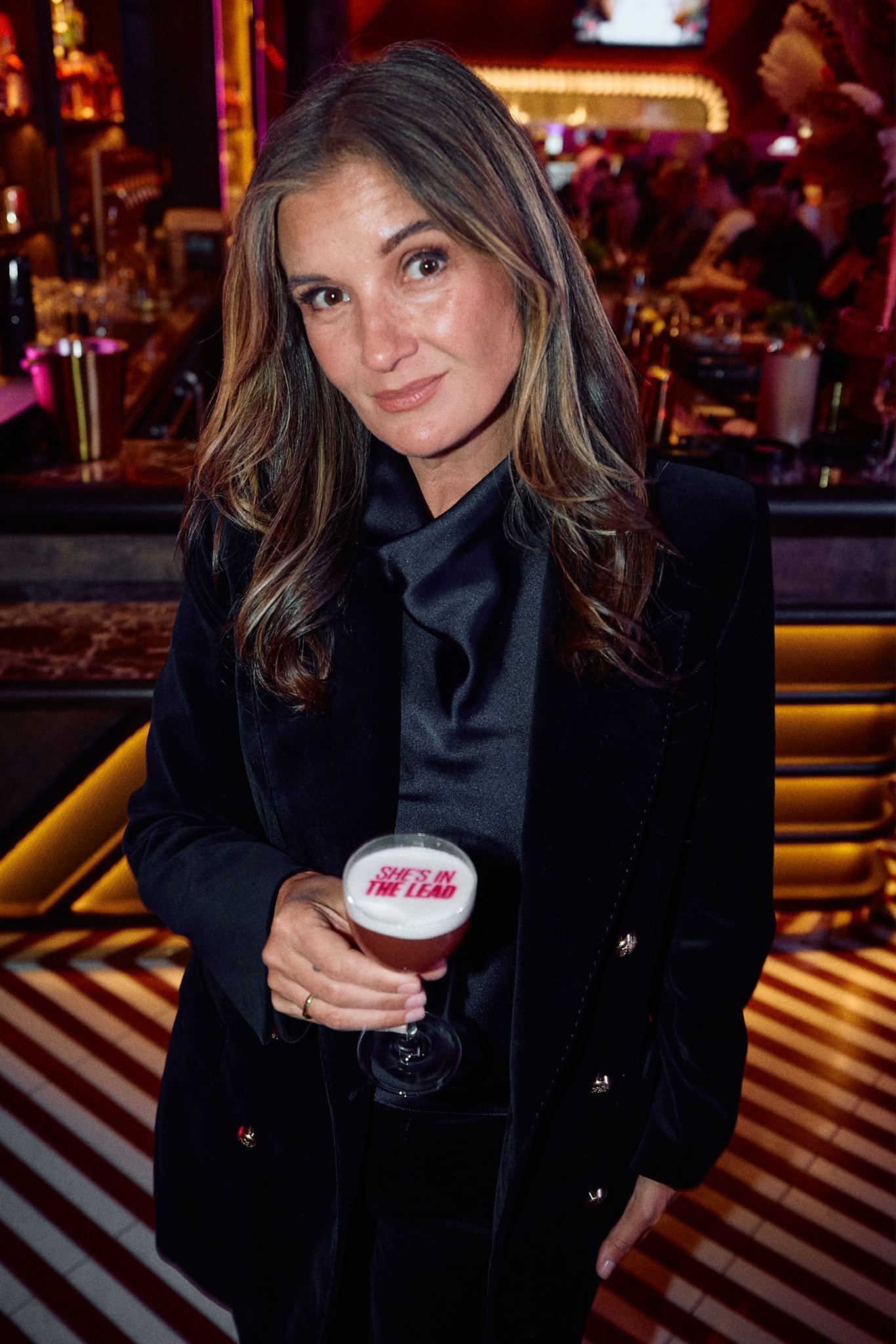 Lizzie Norris in a warmly lit hospitality venue holding a cocktail